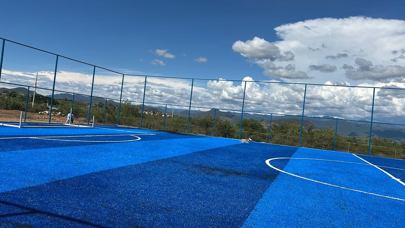 pasto sintético azul en cancha multiusos deportiva con barandal y vista panorámica