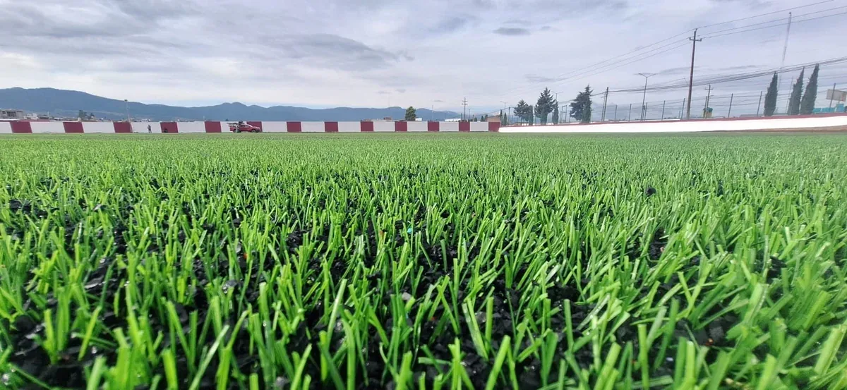 Pasto sintético a nivel de piso en la cancha de soccer del Campo Deportivo Chignahuapan, Puebla, con postes de iluminación al fondo