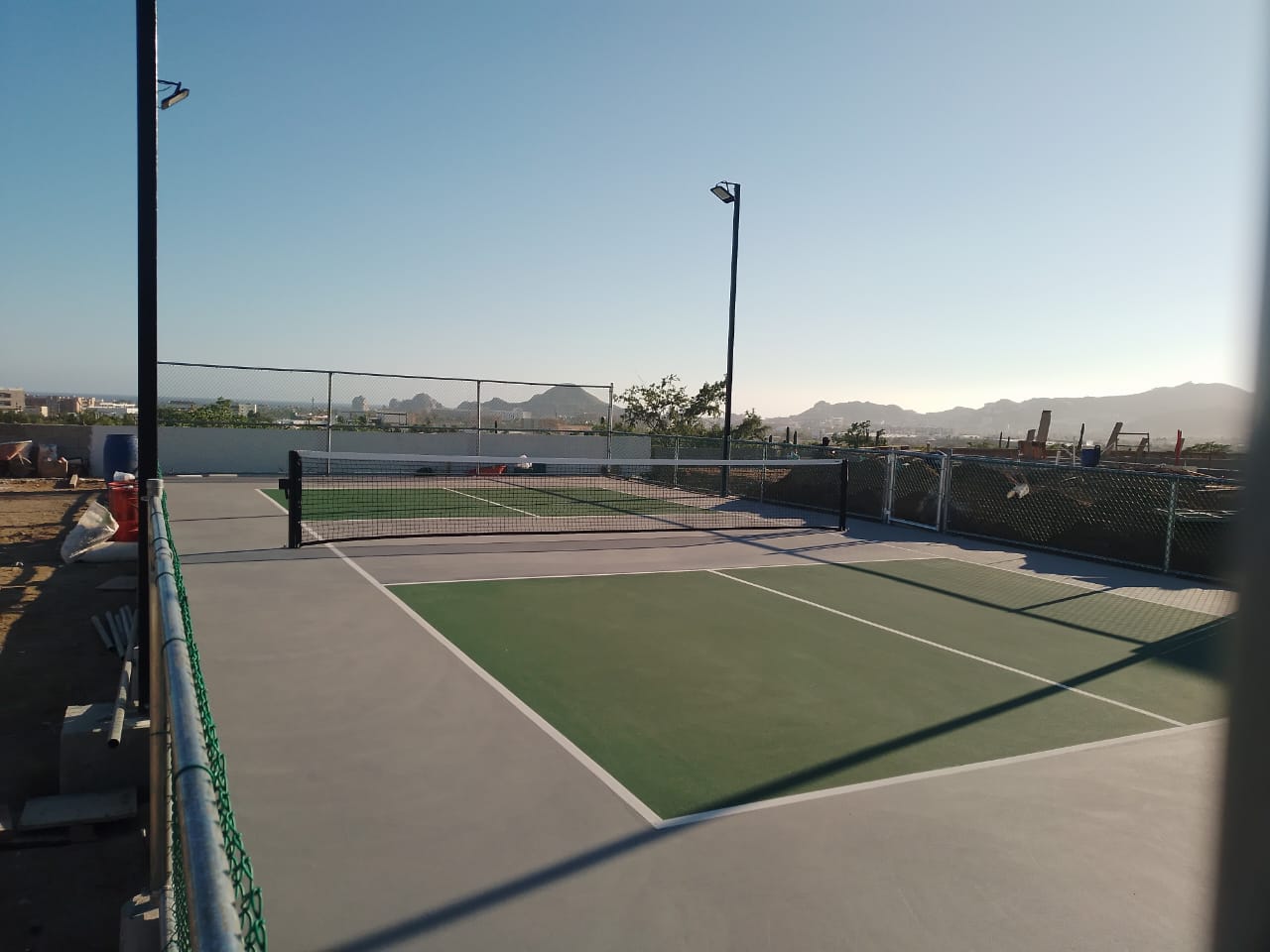 Canchas de pickleball en construccion en club deportivo de Los Cabos con montanas postes de iluminacion LED y cercado perimetral