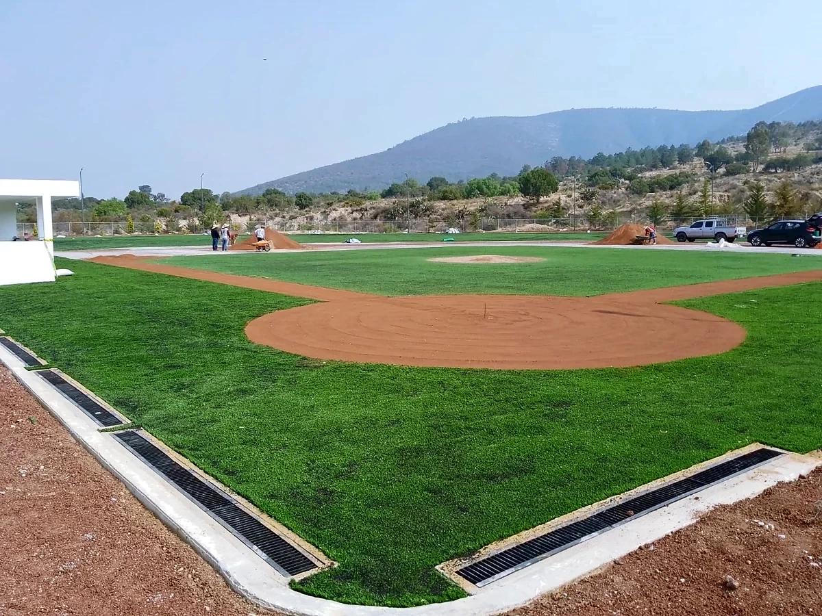 Infield de pasto sintético con montículo y zonas de tierra en construcción en el Campo Felipe Ángeles, Santiago Tenango, Puebla