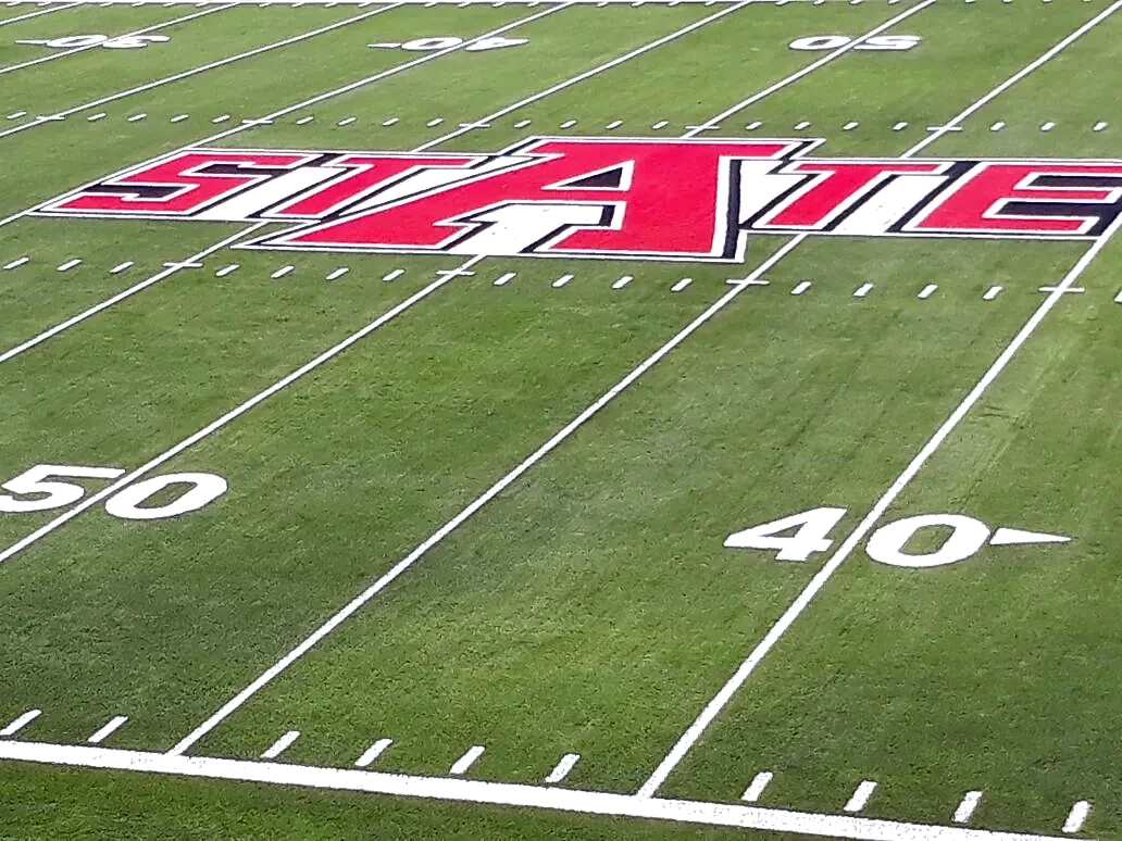Logotipo STATE cortado e integrado en el pasto sintético del campo de fútbol americano de Arkansas State University, Querétaro