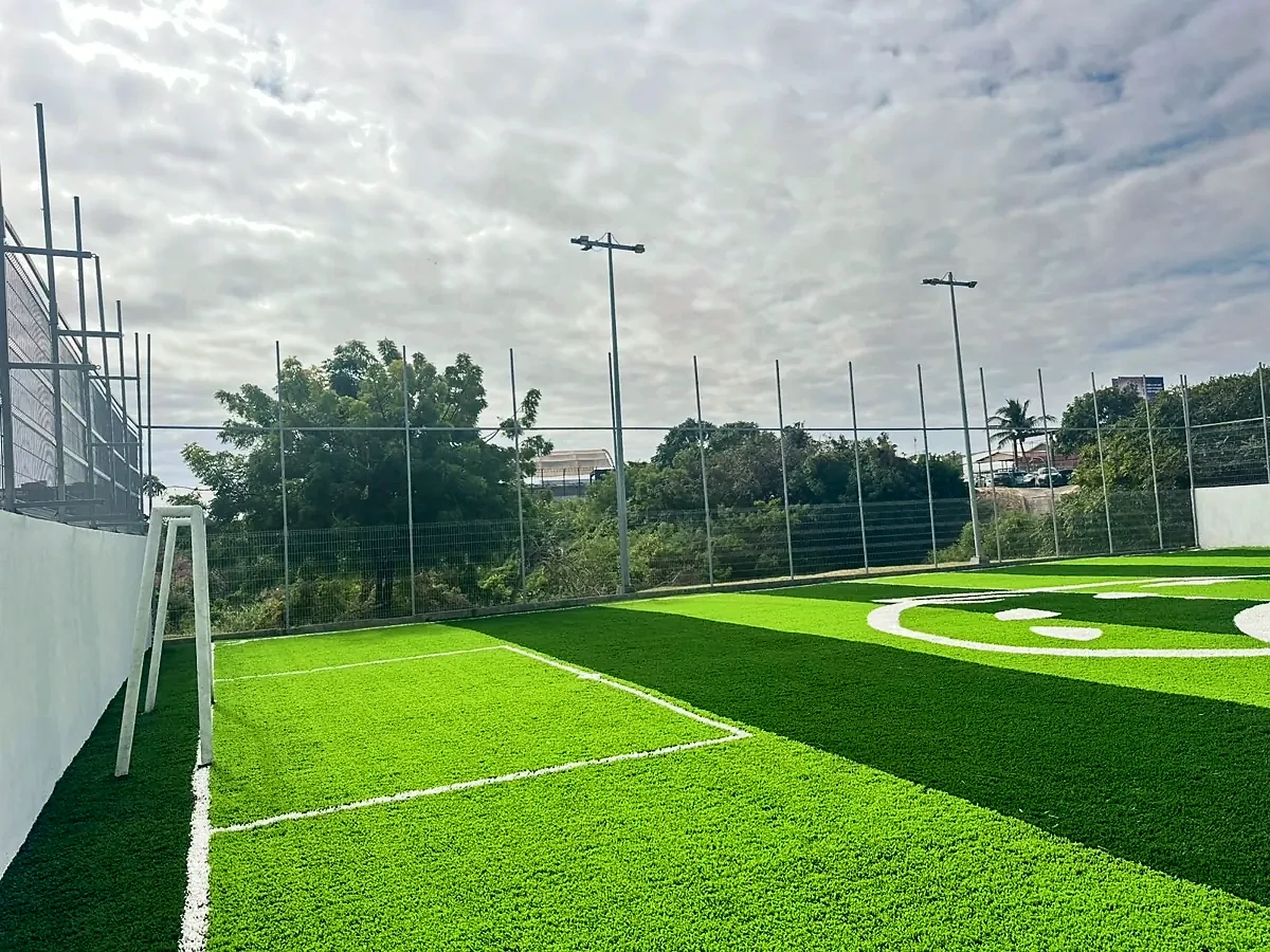 Lateral de una cancha de pasto sintético con malla perimetral y postes de alumbrado en una institución educativa de Tampico