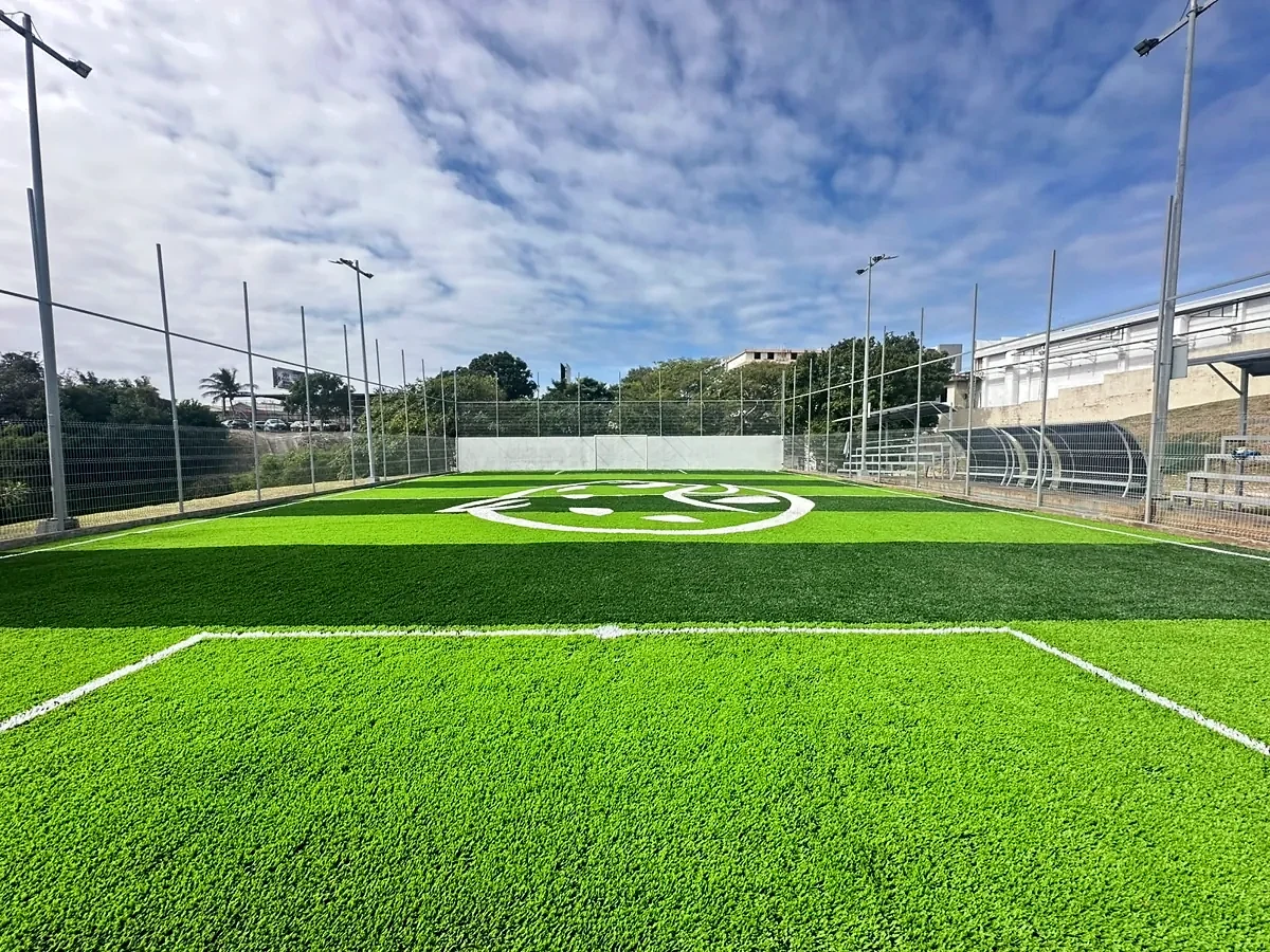 Vista general de la cancha de fútbol 7 con pasto sintético a franjas, logotipo y gradas en la UNE, Tampico